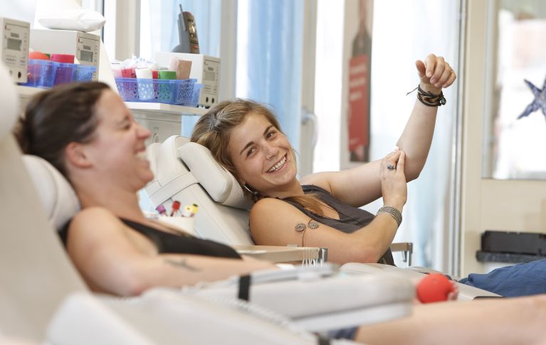 Das Bild zeigt zwei lachende Frauen während der Blutspende.
